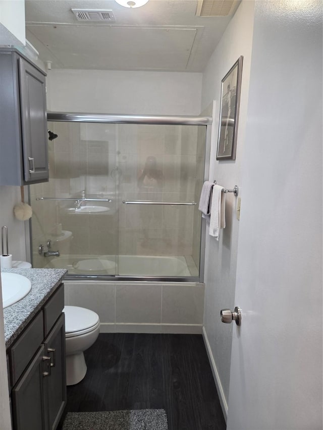 bathroom with combined bath / shower with glass door, visible vents, toilet, wood finished floors, and vanity