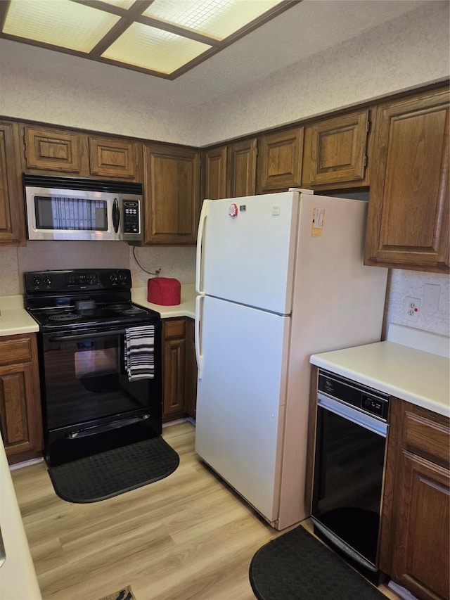 kitchen featuring stainless steel microwave, black electric range oven, light countertops, freestanding refrigerator, and light wood-type flooring