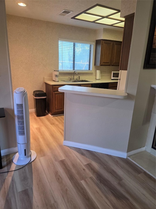 kitchen featuring a sink, light wood-style floors, visible vents, light countertops, and baseboards