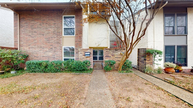 property entrance with stucco siding, fence, a gate, and brick siding