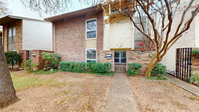 view of property featuring a gate, brick siding, fence, and stucco siding