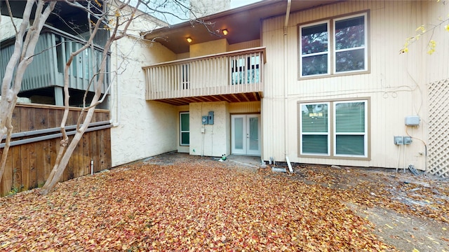back of house featuring fence, french doors, a balcony, and stucco siding