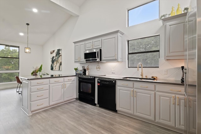 kitchen featuring backsplash, light wood-type flooring, a sink, black appliances, and a peninsula