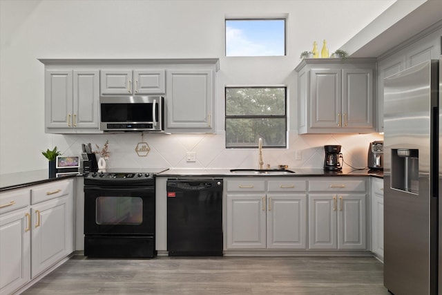 kitchen with decorative backsplash, dark countertops, a sink, black appliances, and light wood finished floors