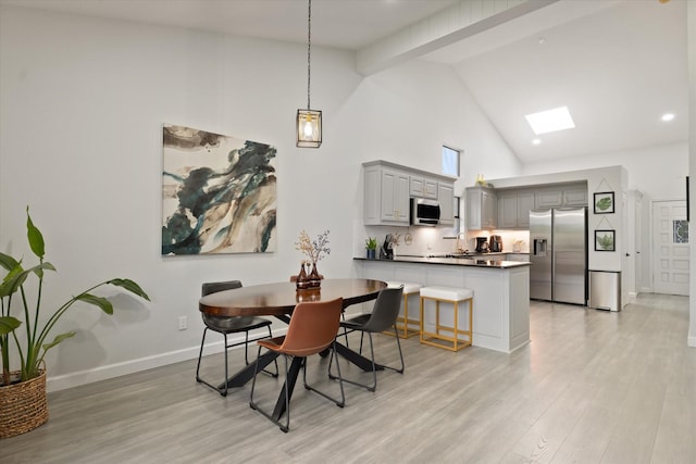 dining area featuring high vaulted ceiling, baseboards, and light wood-type flooring