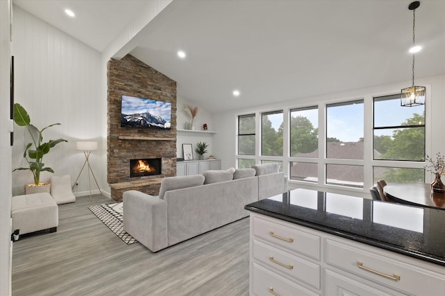 living room featuring vaulted ceiling with beams, a stone fireplace, light wood-style flooring, and a wealth of natural light