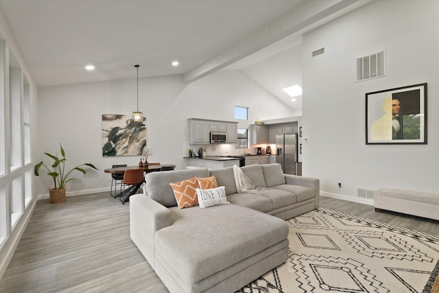 living room with baseboards, light wood finished floors, high vaulted ceiling, and visible vents