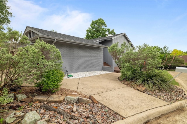 view of side of property featuring entry steps, a shingled roof, and brick siding