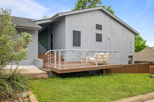 rear view of house featuring fence, roof with shingles, brick siding, a deck, and a yard