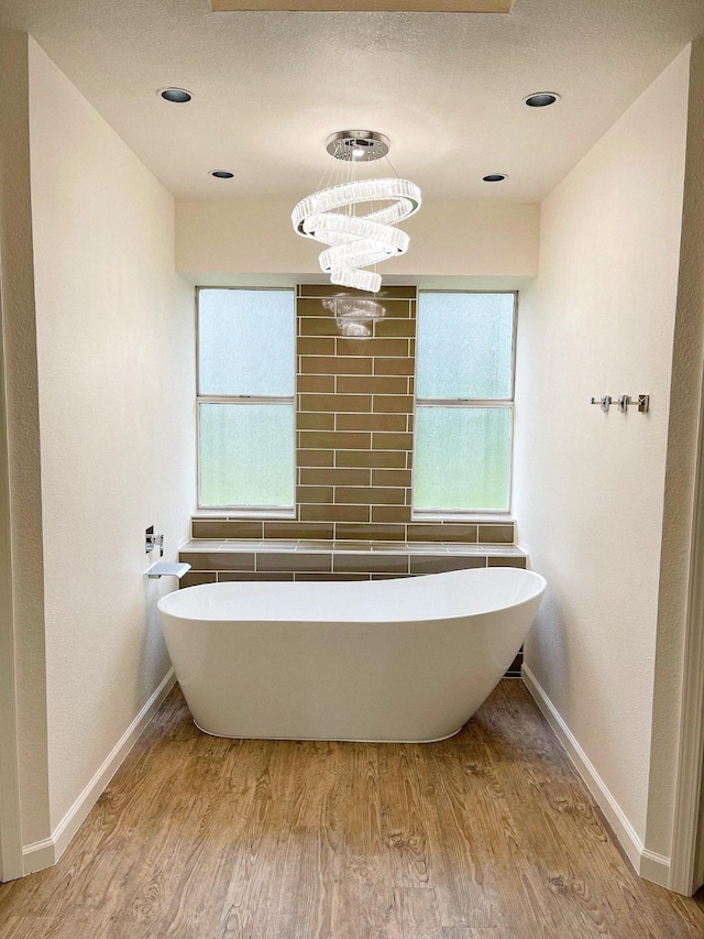full bath featuring plenty of natural light, a freestanding bath, wood finished floors, and baseboards