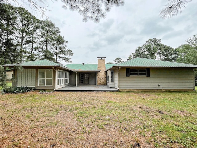 rear view of house with a chimney, a patio, a yard, and metal roof