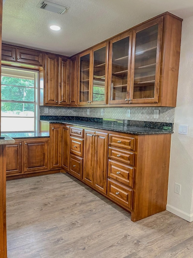 kitchen featuring light wood finished floors, brown cabinets, visible vents, backsplash, and a textured ceiling