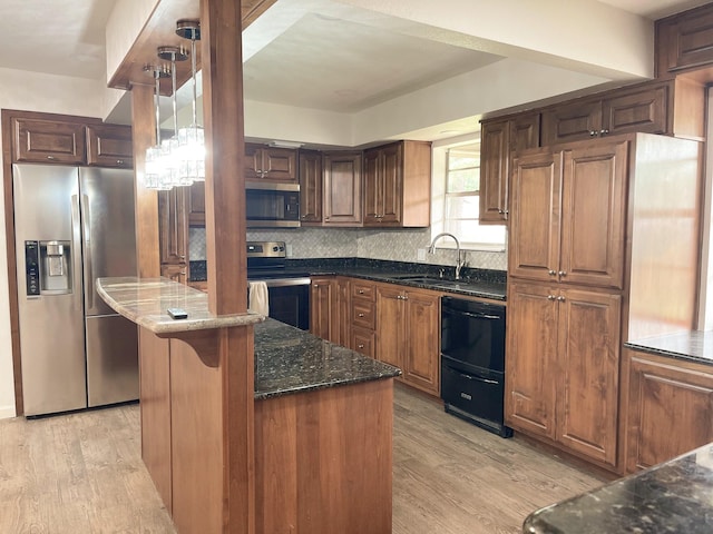 kitchen with dark stone counters, light wood-type flooring, stainless steel appliances, and a sink