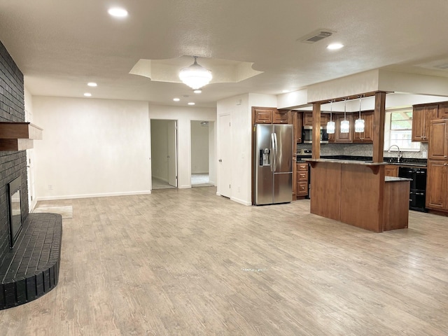 kitchen featuring stainless steel appliances, a fireplace, a center island, dark countertops, and open floor plan