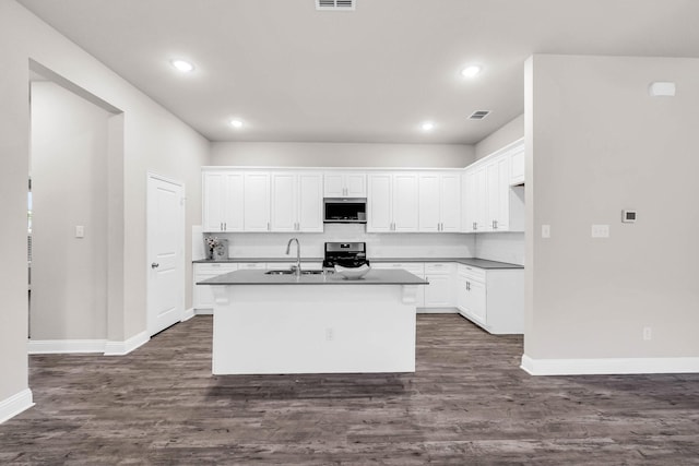 kitchen featuring appliances with stainless steel finishes, white cabinets, dark countertops, baseboards, and a center island with sink