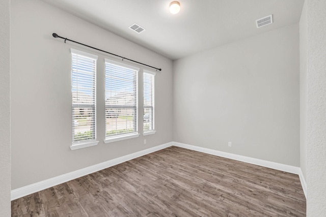 spare room with baseboards, visible vents, and wood finished floors