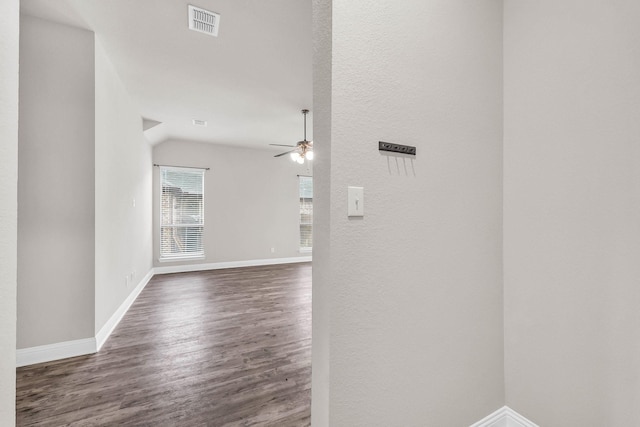 hall featuring a textured wall, visible vents, baseboards, vaulted ceiling, and wood finished floors