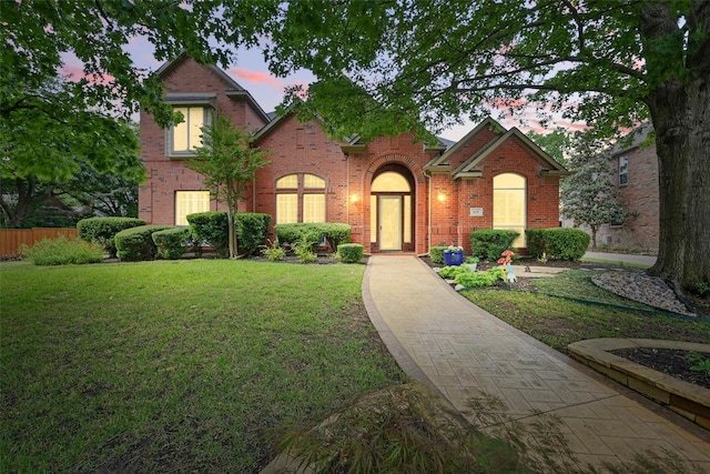 view of front of home with brick siding, fence, and a front lawn