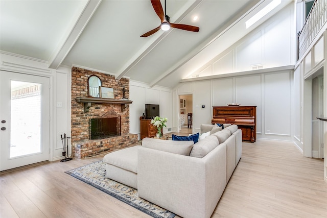 living area featuring a decorative wall, beamed ceiling, light wood-type flooring, a ceiling fan, and a brick fireplace