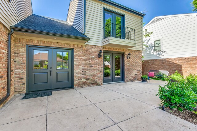 property entrance with french doors, brick siding, roof with shingles, and a patio