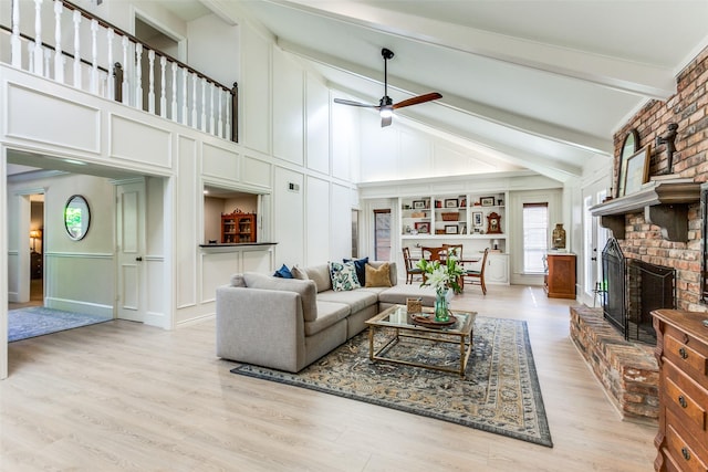 living area featuring a fireplace, high vaulted ceiling, ceiling fan, light wood-style flooring, and a decorative wall