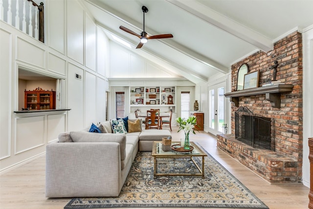 living area with light wood finished floors, beamed ceiling, a decorative wall, a fireplace, and a ceiling fan