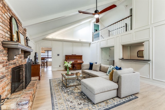 living room featuring beamed ceiling, light wood-style flooring, a decorative wall, a brick fireplace, and ceiling fan