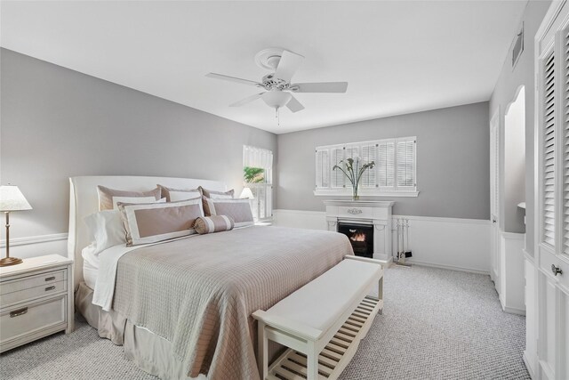 bedroom featuring visible vents, a lit fireplace, ceiling fan, and light carpet