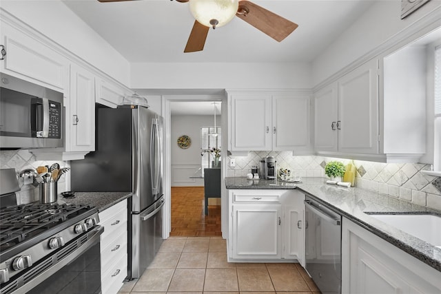 kitchen featuring decorative backsplash, ceiling fan, white cabinetry, dark stone countertops, and appliances with stainless steel finishes