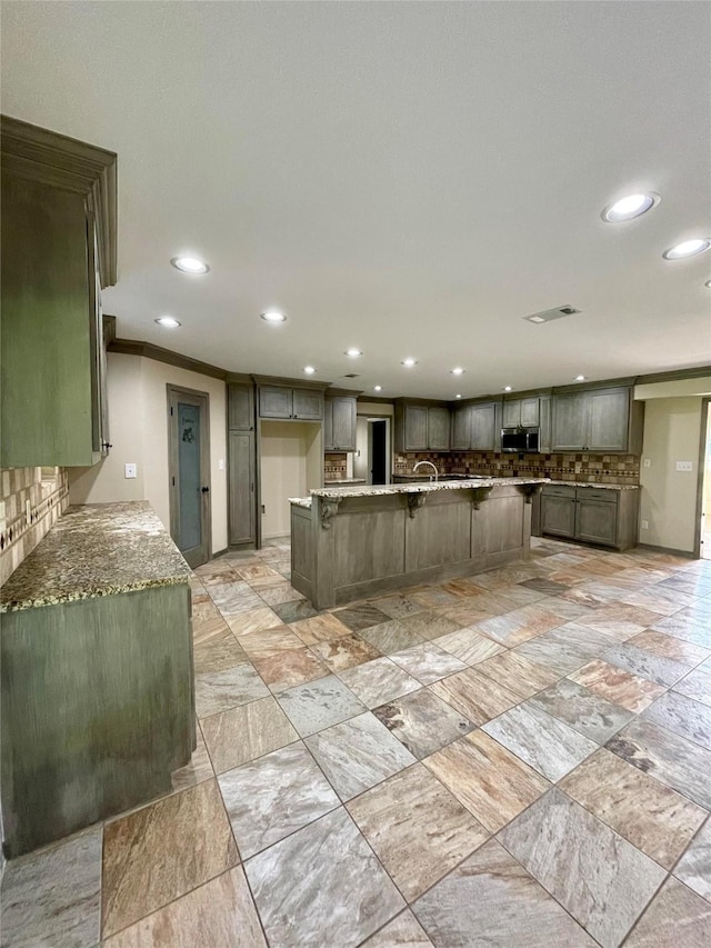 kitchen featuring visible vents, a breakfast bar area, recessed lighting, stainless steel microwave, and stone counters