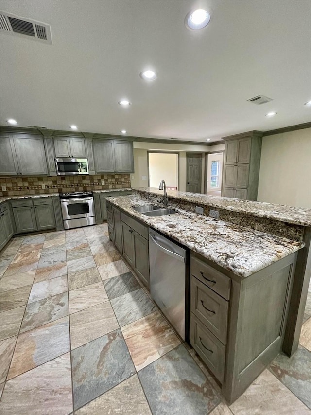 kitchen with visible vents, tasteful backsplash, light stone countertops, a sink, and stainless steel appliances