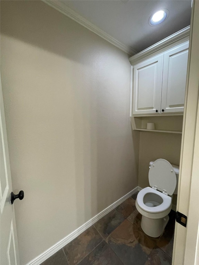 bathroom featuring baseboards, ornamental molding, toilet, and stone finish flooring