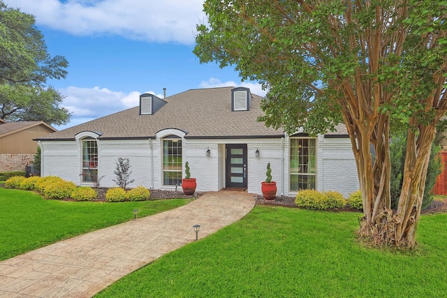 french country home featuring a front yard, roof with shingles, and brick siding