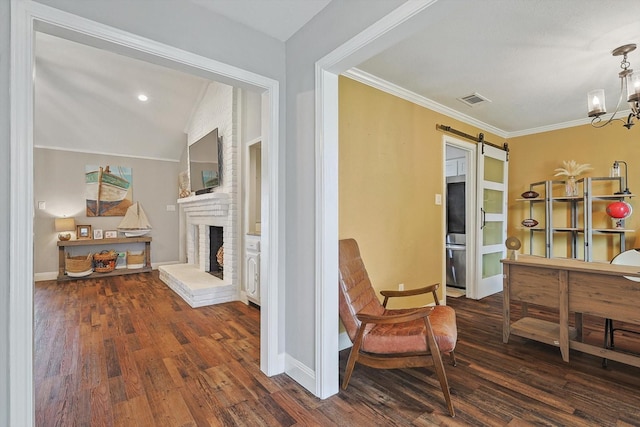 living area featuring wood finished floors, a barn door, ornamental molding, a brick fireplace, and visible vents