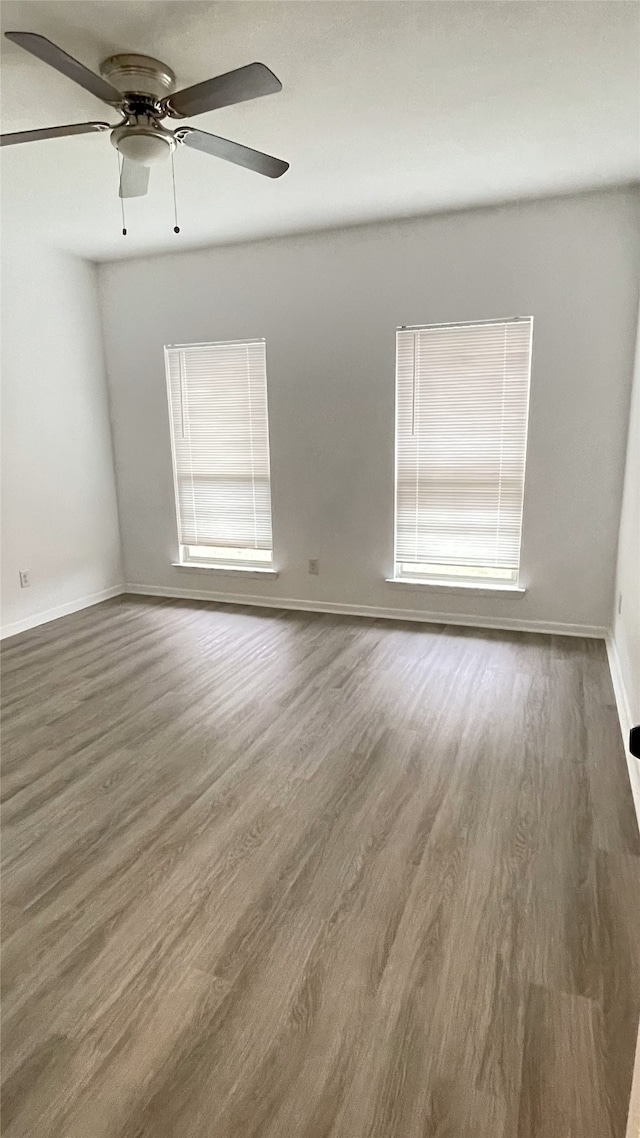 spare room with wood finished floors, a ceiling fan, and baseboards