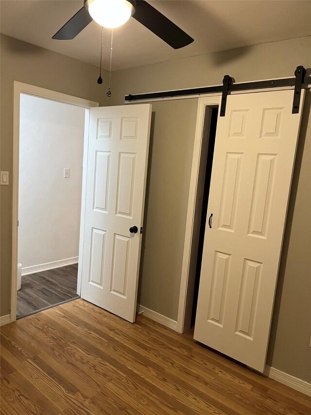 509 W 3rd St, Claude, TX 79019 - unfurnished bedroom featuring wood finished floors, a barn door, ceiling fan, and baseboards