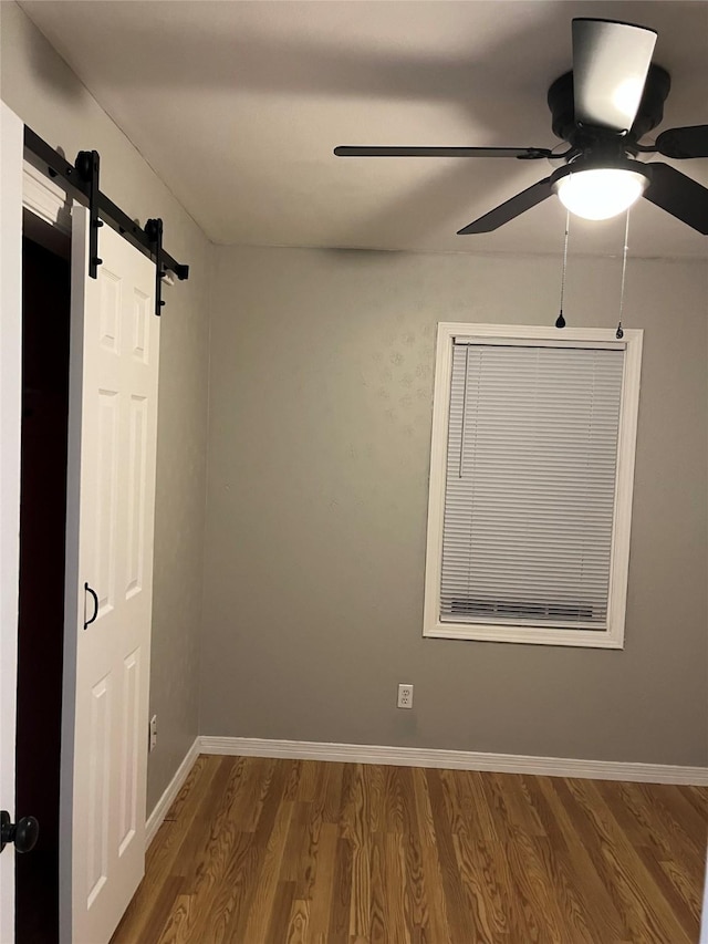509 W 3rd St, Claude, TX 79019 - spare room with baseboards, a barn door, wood finished floors, and a ceiling fan