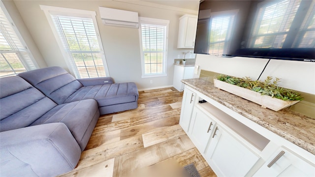 living area with light wood-style flooring, a wealth of natural light, a wall mounted AC, and baseboards