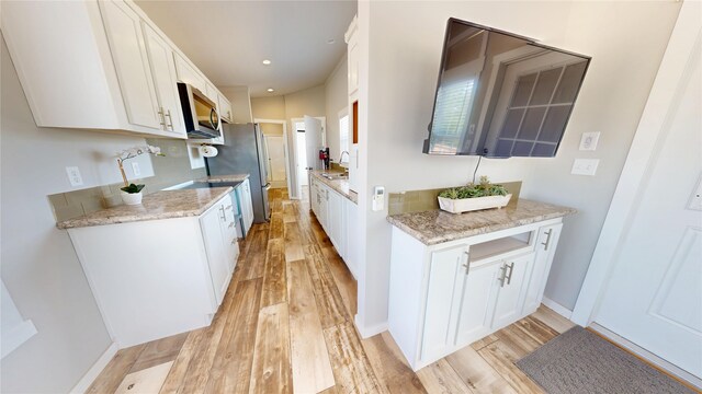 kitchen featuring white cabinetry, a sink, appliances with stainless steel finishes, light wood-style floors, and baseboards