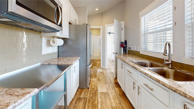 kitchen with a sink, light wood-style floors, backsplash, white cabinets, and appliances with stainless steel finishes