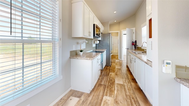 kitchen featuring white cabinets, light wood-style flooring, a sink, stainless steel appliances, and baseboards