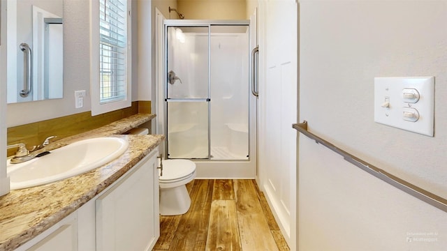bathroom featuring wood finished floors, a shower with door, toilet, and vanity