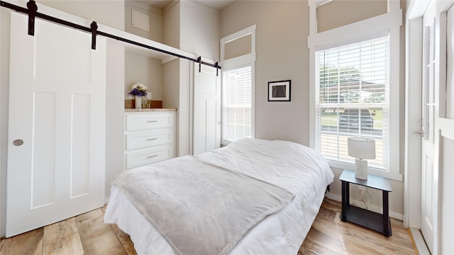 bedroom featuring a barn door, light wood-style flooring, and multiple windows