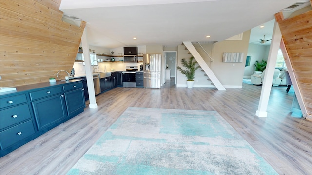 unfurnished living room featuring a sink, light wood finished floors, stairs, and a ceiling fan