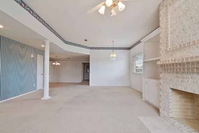 unfurnished living room with decorative columns, light colored carpet, ceiling fan with notable chandelier, and a brick fireplace