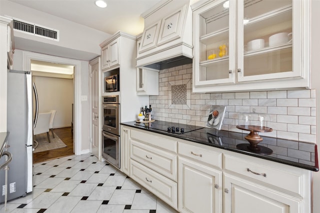kitchen featuring glass insert cabinets, stainless steel appliances, dark countertops, visible vents, and premium range hood