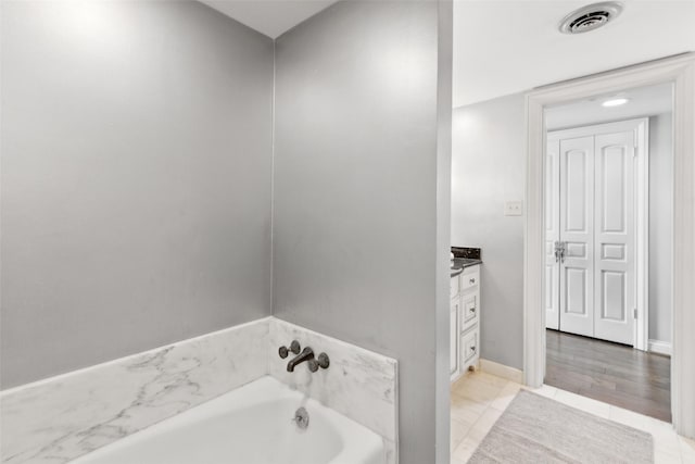 bathroom with a garden tub, vanity, visible vents, and baseboards