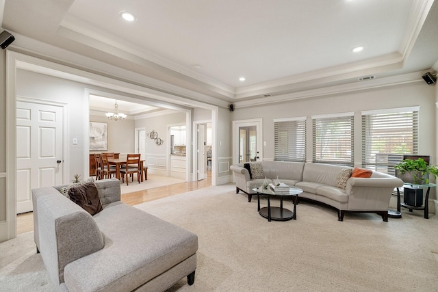 living area featuring a notable chandelier, light carpet, a raised ceiling, a decorative wall, and ornamental molding