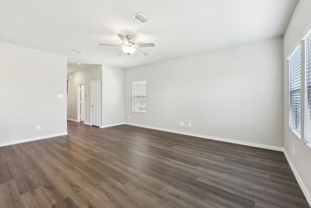 unfurnished room with dark wood-style floors, visible vents, ceiling fan, and baseboards