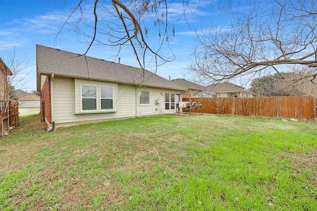 back of house with a yard, a shingled roof, and a fenced backyard